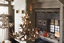 a contemporary chalet living room with a concrete fireplace, neutral furniture, antler chandeliers and colorful pillows