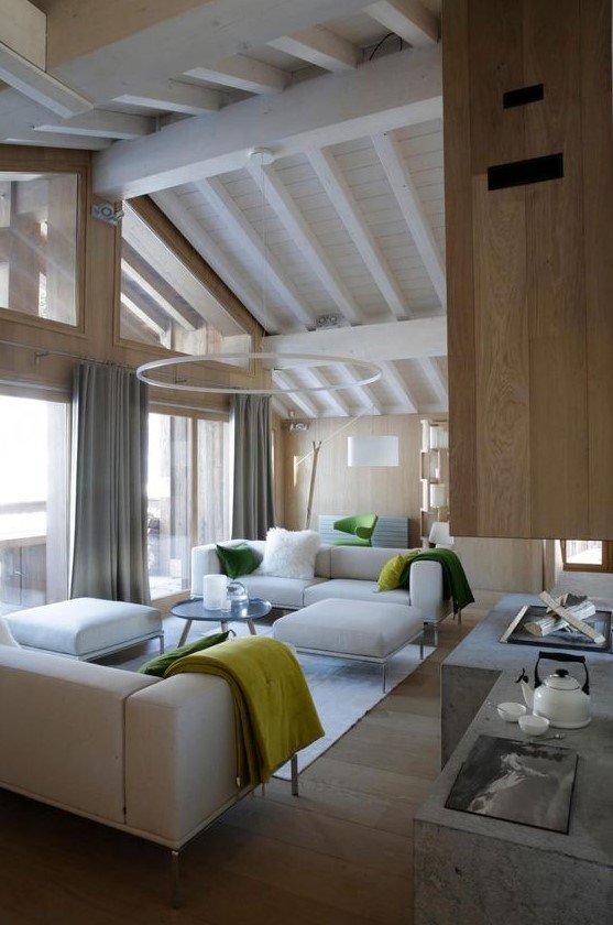 A contemporary light filled chalet living room with neutral furniture, a glazed wall and an open fireplace of concrete