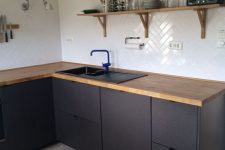 a contemporary matte black kitchen with light stained wooden countertops and matching wooden shelves looks chic