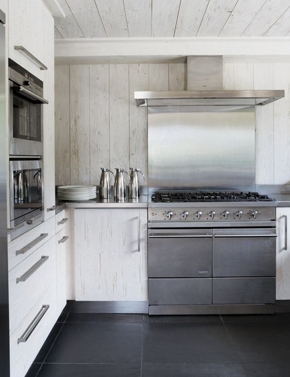 a contemporary white chalet kitchen all clad with wood, with stainless steel appliances is laconic and chic