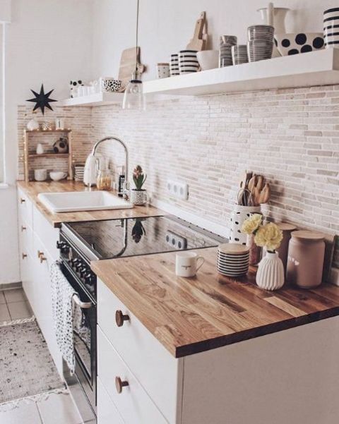 a contemporary white kitchen with light stained butcherblock countertops, a pendant lamp and white floating shelves