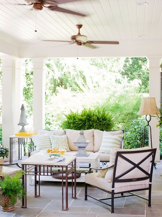 a cozy summer porch with ceiling fans, comfy upholstered furniture, a floor lamp and some tables