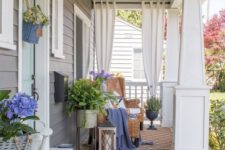 a cozy summer porch with wicker futniture, potted greenery and flowers, a jute rug, a dresser and some curtains