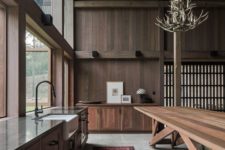 a dark chalet kitchen clad with wood, with wooden furniture and antler chandeliers plus a glazed wall