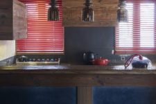 a dark chalet kitchen with sleek wooden furniture, a blue kitchen island, red shades, pendant lamps