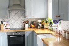a dove grey kitchen with light stained butcherblock countertops and copper touches plus a geometric white tile backsplash