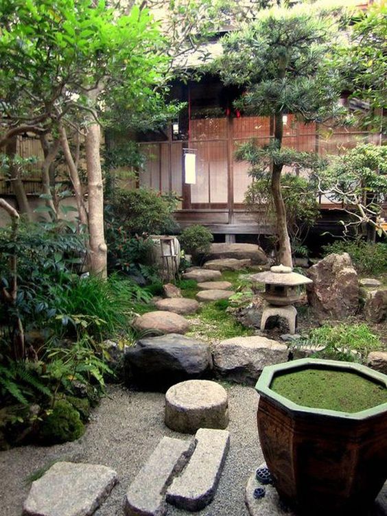 a fantastic Japanese backyard with rocks, a stone lantern, greenery and trees and a bowl with greenery inside