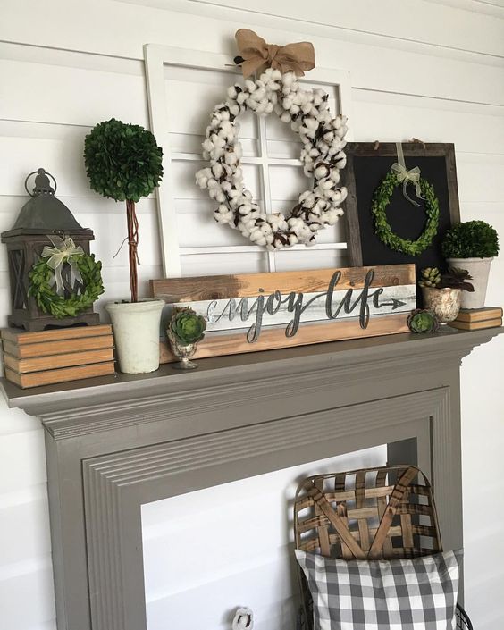 a farmhouse mantel with a pallet, a cotton wreath, greenery wreaths and greenery in planters