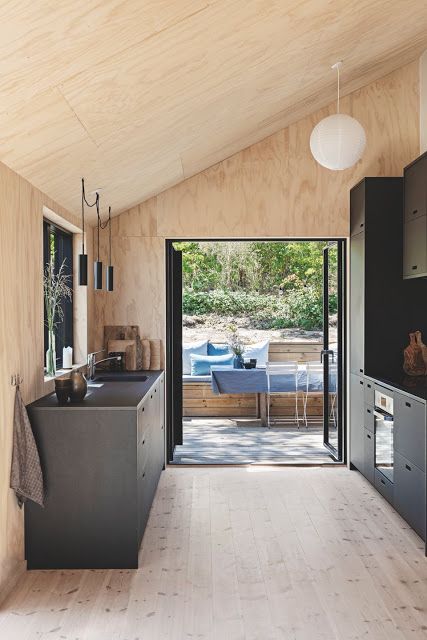 A light colored chalet kitchen clad with wood and plywood, with black cabinets and stylish pendant lamps