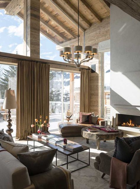 A light filled chalet living room with a neutral fireplace, leather seating furniture, a coffee table of wood and metal and neutral textiles