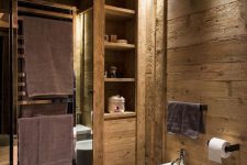 a lovely chalet bathroom clad with textural wood, with white appliances, black holders and built-in lights
