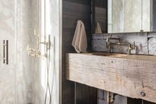 a lovely chalet bathroom done with textural and aged wood, with white stone, antique brass fixtures and a mirror