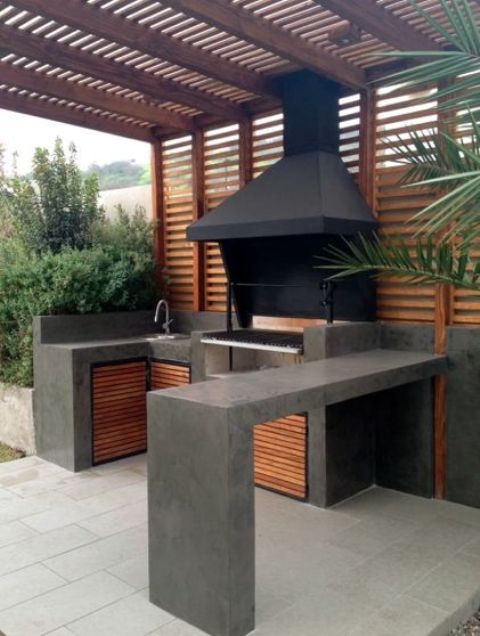 a minimalist bbq area of dark concrete and wood, with a grill and a sink plus a concrete countertop for eating