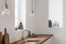 a minimalist white kitchen with dark stained chevron butcherblock countertops and pendant bulbs over the space