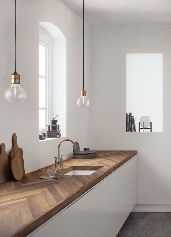 a minimalist white kitchen with dark stained chevron butcherblock countertops and pendant bulbs over the space