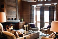 a modern cozy chalet living room with stained walls, a fireplace, plaid seating furniture, a side table and candles plus plaid curtains