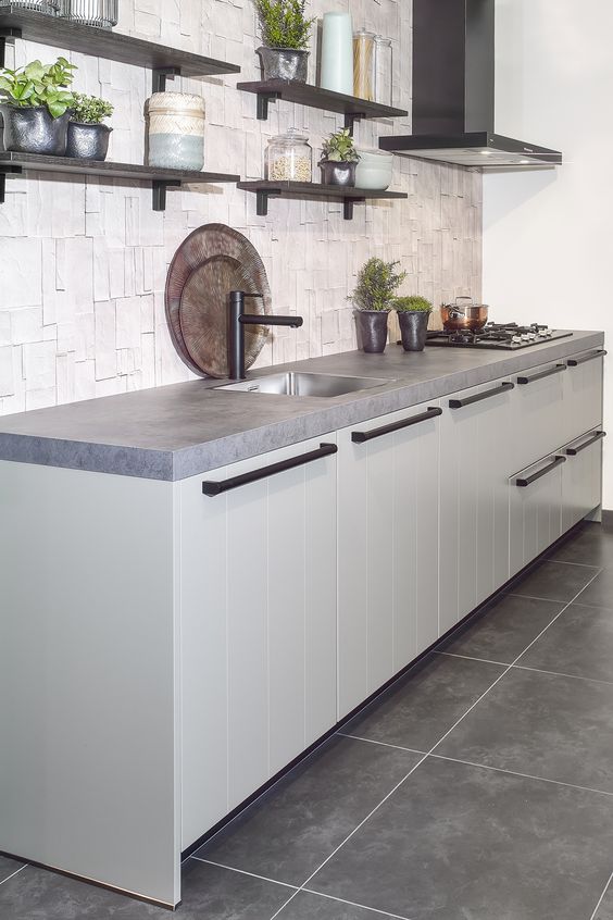 a modern kitchen with grey cabinets, concrete countertops and a catchy backsplash plus dark shelves