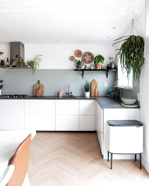 a modern kitchen with sleek white cabinets, a black concrete countertops and a grey backsplash plus lots of greenery