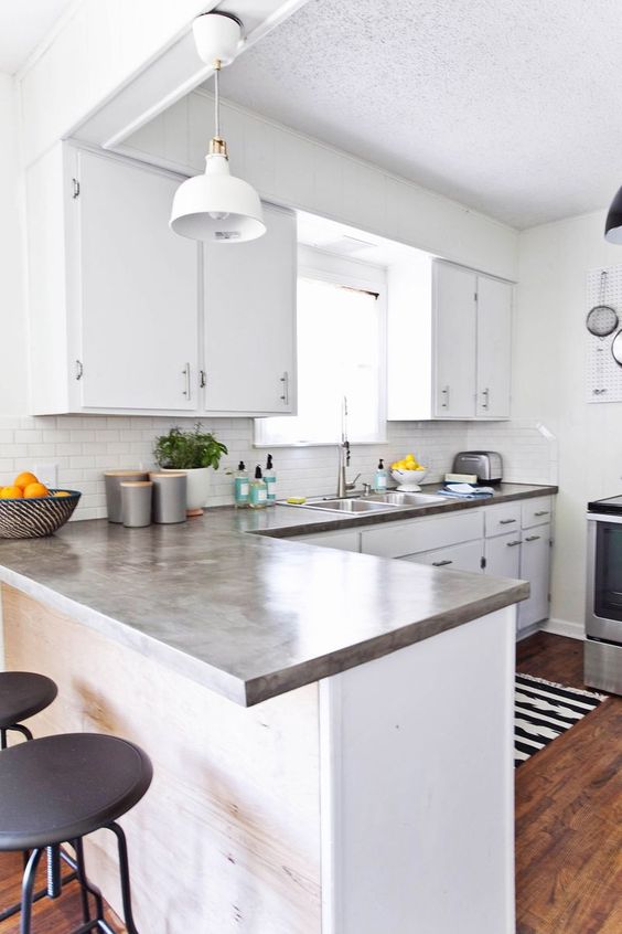 a modern white kitchen with concrete countertops, a white subway tile backsplash and a pendant lamp
