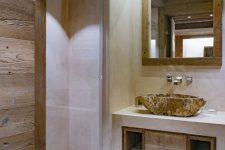 a neutral and contemporary chalet bathroom done with wood and with white concrete, with a stone sink and a mirror in a wooden frame