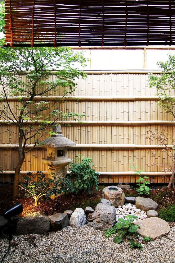 a peaceful Japanese garden with rocks and pebbles, a stone lantern, two trees, greenery and lights is very chic