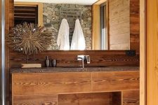 a pretty chalet bathroom clad with wood, with a built-in vanity, a large mirror, a basket for storage and a pretty artwork
