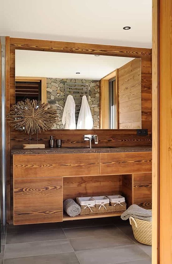 A pretty chalet bathroom clad with wood, with a built in vanity, a large mirror, a basket for storage and a pretty artwork