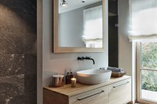 a pretty modern chalet bathroom done with blonde wood, grey stone tiles, a floating vanity, a chic sink and a large mirror