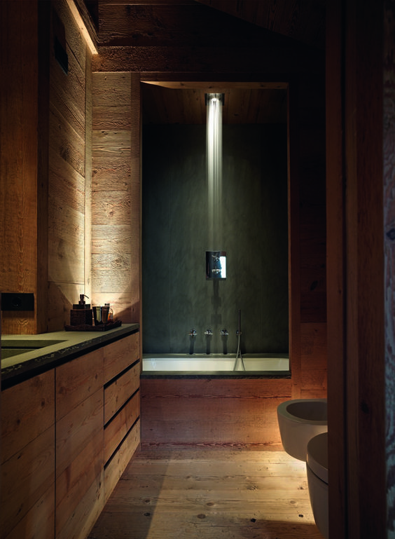 A relaxing chalet bathroom clad with wood, with a rainshower and a bathtub, a built in vanity and built in lights