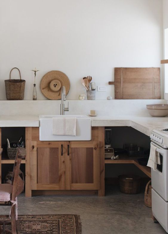 a rustic neutral kitchen with wooden cabinets and open shelves and a white concrete countertop and backsplash