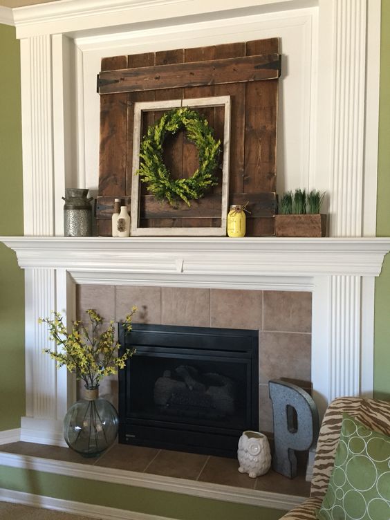 a rustic summer mantel with a greenery wreath, greenery in a planter, a yellow jar, a churn and a pallet wood piece