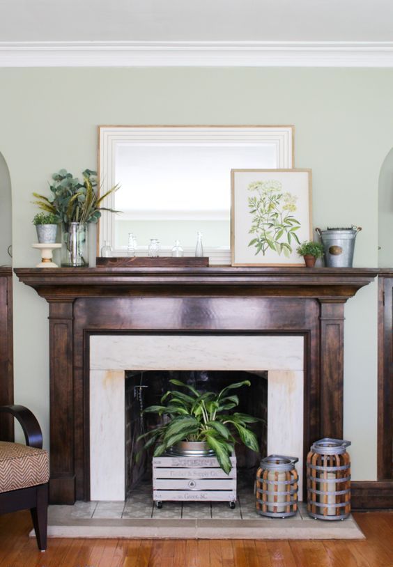 a rustic summer mantel with a vintage artwork, greenery arrangements, crates, bottles and candle lanterns