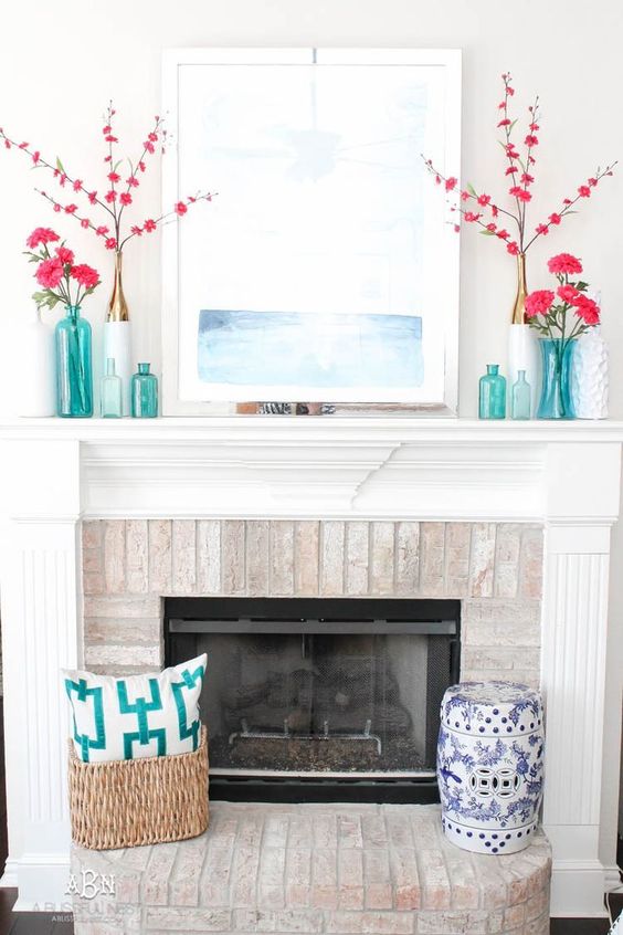 a seaside summer mantel with bright pink blooms, turquoise vases and bottles, a seascape and a basket