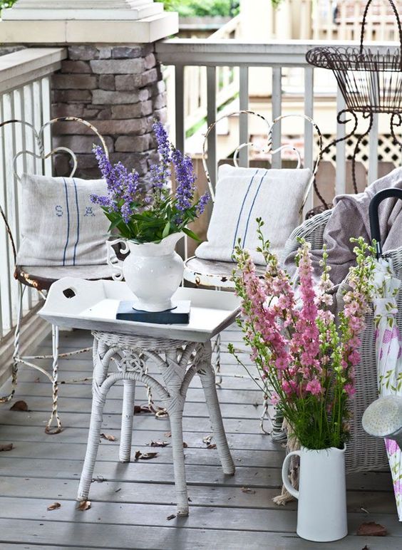 a shabby chic summer porch with metal and wicker furniture and bright floral arrangements