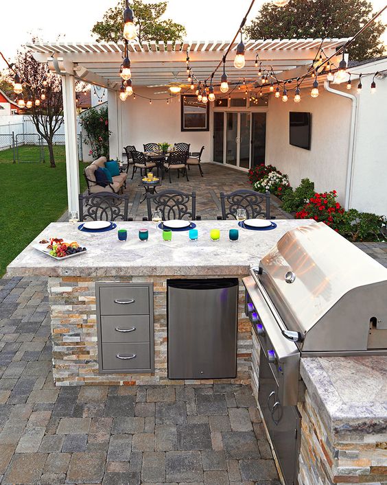 a simple rustic bbq area built of stone, with storage units and a grill plus an eating zone