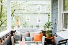 a simple summer porch with a white wicker loveseat, white stools, a wooden chair and some lights around