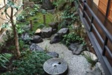 a small Japanese space with a stone bowl, greenery and moss, a bamboo fountain, a low tree and rocks