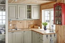 a small rustic chalet kitchen with grey cabinets, wooden countertops, wood plank walls and built-in lights