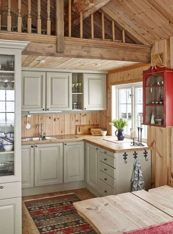A small rustic chalet kitchen with grey cabinets, wooden countertops, wood plank walls and built in lights