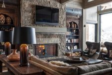 a stylish chalet living room clad with wood, with a stone fireplace, boho and modern furniture and round chandeliers