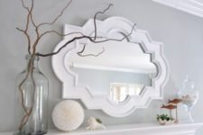 a summer coastal mantel with seashells, greenery, fish figurines, branches and a vintage mirror