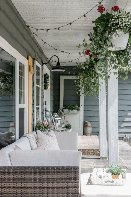 a summer farmhouse porch with wicker furniture, potted greenery and blooms, an old door and chair plus potted blooms