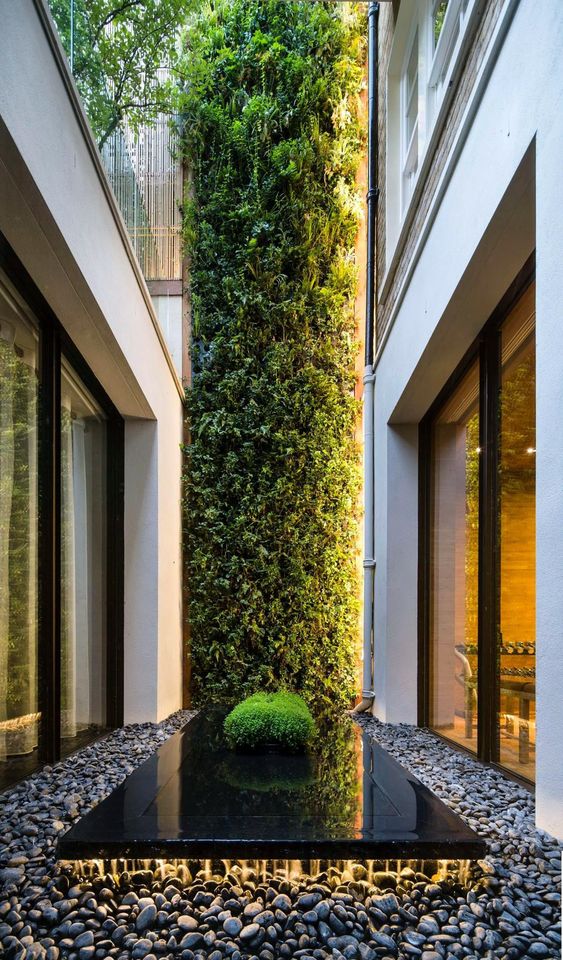 a super chic indoor courtyard with pebbles, a black sleek platform and a greenery wall going up to the top