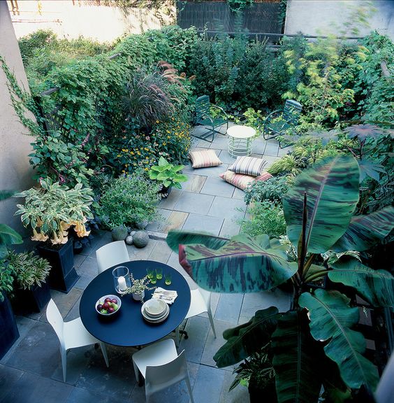 a townhouse oasis with stone tiles, a contemporary dining set with a round table, growing greenery and plants and some pillows
