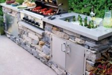 a traditional outdoor bbq area with a stone unit, a concrete countertop, a grill, a cooking zone and a drink cooler
