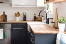 a trendy two tone kitchen in black and white and with light stained butcherblock countertops and matte black faucets
