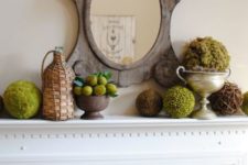 a vintage rustic mantel with a wooden mirror, moss and greenery balls, lemons and a bottle