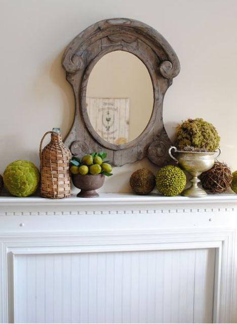 a vintage rustic mantel with a wooden mirror, moss and greenery balls, lemons and a bottle