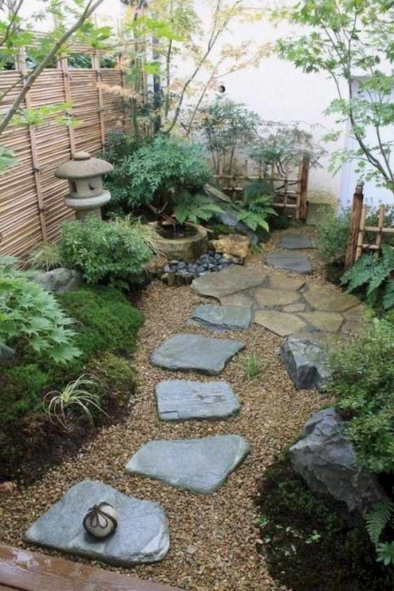 a welcomign Japanese courtyard with rocks, greenery, moss, a stone lantern and a bamboo fountain plus a low fence