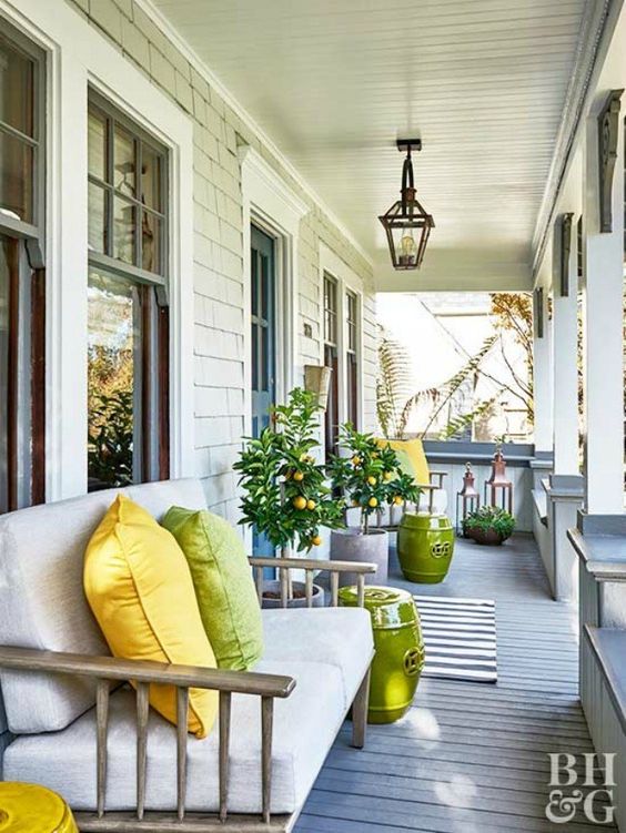 a welcoming summer porch with rattan sofas, large lanterns, green side tables and potted citrus trees